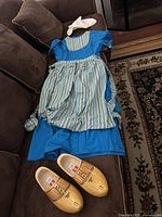 Photo of the complete costume set including dress, striped apron, white fabric hat, and wooden shoes.