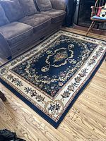 Full photo of the rectangular floral rug on a wooden floor beneath a brown sofa and wooden chairs, showing the overall design and colors.