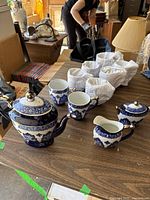 Full view of the teapot, sugar bowl, creamer, and 3 of the 8 mugs with the remaining mugs wrapped in cloth