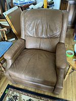 Front view of brown vegan leather recliner chair showing padded armrests and backrest with some creasing and wear.