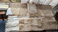Full view of assorted lace doilies and embroidered table linens in beige, white, and off-white on wooden table