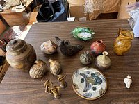 Overall view of the lot arranged on a table showing stoneware quail figures, small vases, glass pitcher, gold figurines, conch shell, and the decorative plate.