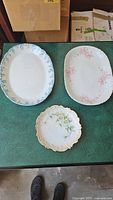 Top-down photo of 2 oval porcelain serving platters with floral patterns and 1 round plate with daisy floral design.