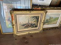 Image showing five framed art pieces stacked together, one prominently an ornate gold frame of Eiffel Tower scene