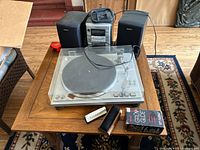 Kenwood KD-2100 turntable with dust cover on wooden table alongside Aiwa stereo system components and accessories.