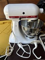 KitchenAid Ultra Power mixer in white with stainless steel bowl and included attachments (whisk, dough hook, flat beater), power cord visible.