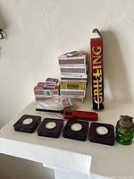 Photo showing four purple glass tea light holders, vintage green glass lighter, red extended lighter, and multiple matchboxes including a large Grill King box.