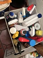 Top view of a box filled with multiple cleaning bottles including spray bottles and other containers, and some cleaning rags.