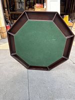 Top view of octagonal poker table with green felt surface and 8 chip/card holder slots around perimeter, set outside on concrete.
