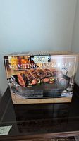 Boxed Kirkland Signature roasting pan and rack front view, showing serving suggestion with roast and vegetables on rack.
