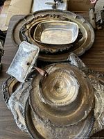 Photo showing stacked silver plated trays and bowls with visible tarnish and ornate floral patterns