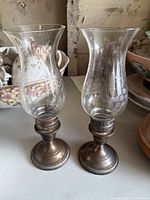 Front view of the two silver plated candelabras with etched glass shades side by side on shelf
