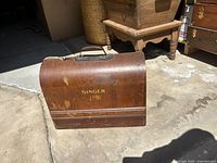 Photo of the wooden carrying case labeled 'SINGER' with handle, showing wear and some scratches.