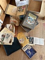 Wide view of various stamp albums, some with stamps, loose stamps in envelopes and small bags, and several books stacked on a wooden floor.