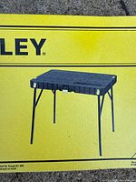 Photo of the fold-up workbench fully unfolded, showing the black plastic top and supporting metal legs.