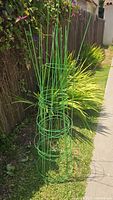 Photo of a green metal garden plant support cage outdoors next to a fence and plants.