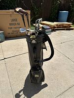 Front side view of the vintage black vegan leather golf bag with gold accents, showing clubs inside and zipper pocket on front.