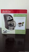 Sunbeam TeaDrop Hot Tea Maker in original retail packaging, showing front box panel with product image and branding.