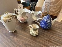 Overview photo showing all the teapots and related porcelain pieces on a wooden surface with a background of furniture items.