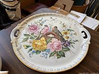 Large round porcelain serving tray with floral and bird motif, decorative handles, and ornate border