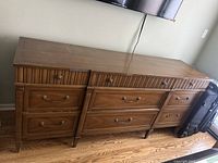 Front view of medium brown wooden dresser with 9 drawers, showing details of handles and carved top drawer panel.