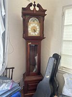 Full view of wooden Emperor grandfather clock showing tall case, base, glass panel with pendulum, and ornate top.