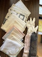 Vintage handkerchiefs and three pairs of gloves including cream, pink, and black, showing lace trims and soft fabric.