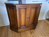 Front view of brown wooden cabinet with two paneled doors and black metal handles.