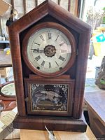 Front view of vintage wooden mantle clock with Roman numeral clock face and eagle motif lower glass door panel.