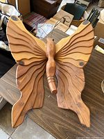 Front view of wooden butterfly sculpture on table showing detailed carved wings, natural wood grain, and antennae.