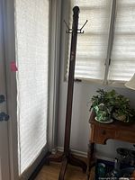 Full view of tall wooden hall tree near window with natural light, showing overall height and design.