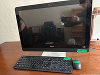 Front view of Dell 23-inch all-in-one PC with wireless keyboard and mouse on a wooden table.