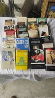 Photo showing all 21 paperback classic novels arranged on a surface, titles clearly visible including Demian, Catch-22, The Magic Mountain, The Outsider.