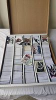 Wide shot of over 2000 hockey cards organized in a large cardboard storage box with several stacks and some loose cards on top.