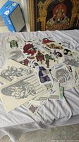 Overview photo showing dozens of medium vinyl decals spread over a cloth surface, depicting dragons, skulls, motorcycles, masks and other designs.