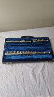 Full view of the metal flute in a blue velvet lined case, showing three separate parts of the flute inside.