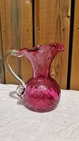 Front side view of textured pink glass pitcher on white surface with wooden background