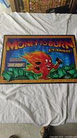 Full view of the slot machine glass art panel with the Money to Burn Classic theme depicting a cartoon flame character and money stacks.