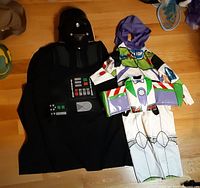 Both costumes laid out: Darth Vader cape and helmet beside Buzz Lightyear suit, wings, hood