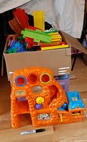 Cardboard box filled with multicolor VTech Go!Go! Smart Wheels track pieces; orange Treasure Mountain playset in front