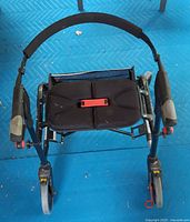 Top view showing padded seat, red release latch, handle grips, front wheels