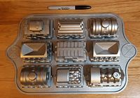 Top view of silver cast aluminum pan with nine detailed train car molds, marker for scale