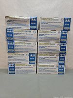Photo showing 10 boxes of Ronco Care blue pleated masks stacked in two columns of five boxes each.
