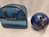 Blue Bonanza bowling ball with finger holes and serial number alongside blue carrying case with handle and stripes