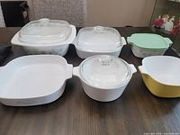 Photo of six Corning Ware casserole dishes on table, various shapes and lid types, some with Blue Cornflower pattern