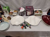 Photo showing an assortment of kitchenware and home decor items on a table including bowls, figurines, and boxed products.