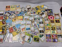 Top view of a large collection of Pokémon cards spread out, all in clear protective sleeves, showing various Pokémon and Trainer cards.