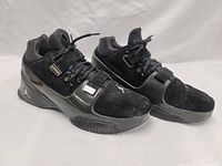 Side angle view showing the black suede and glossy synthetic materials, mid-top design, strap across midfoot, and Jumpman logo on heel.