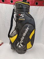Full view of the TaylorMade R5 Hundred Series golf staff bag showing black body with yellow accents and multiple pockets.