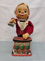Front view of vintage 1960's Rosko bartender toy showing the figure holding a shaker and colorful tin litho base labeled 'BARTENDER'.